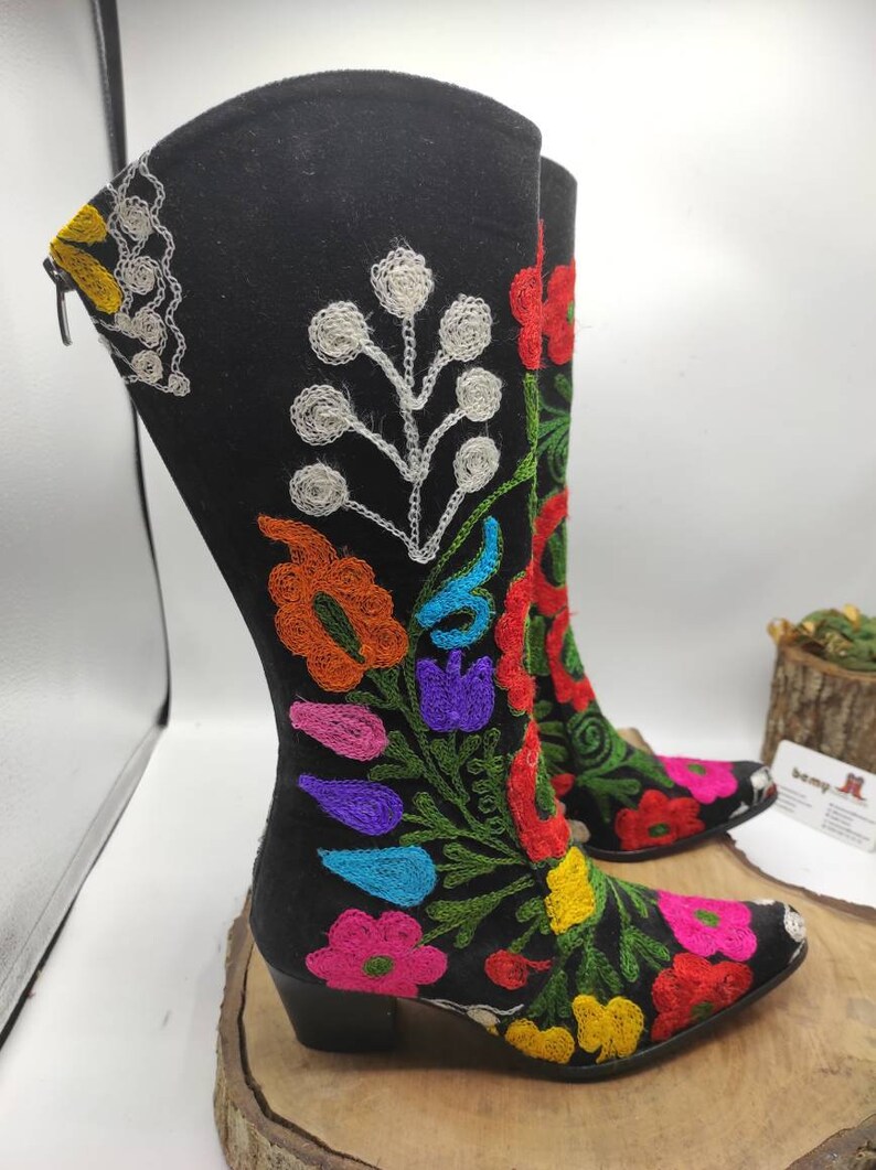 May include: Black suede boots with colorful floral embroidery. The boots have a pointed toe and a block heel.