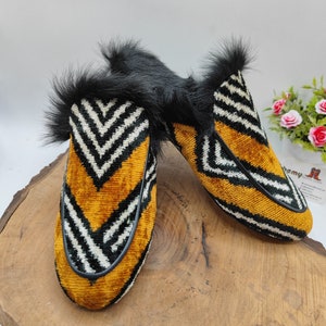 Puede incluir: Un par de zapatillas de terciopelo a rayas blancas y negras con un acento amarillo y ribete de piel negra.