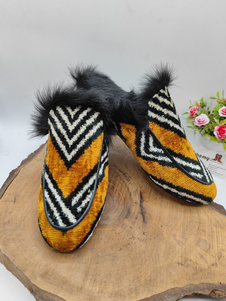 Puede incluir: Un par de zapatillas de terciopelo a rayas blancas y negras con un acento amarillo y ribete de piel negra.