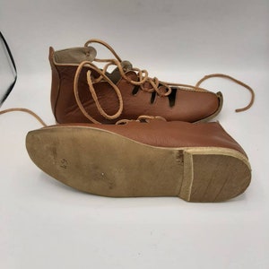 May include: Brown leather sandals with laces and cutouts. The sandals have a brown leather sole with the number 37 written on it.
