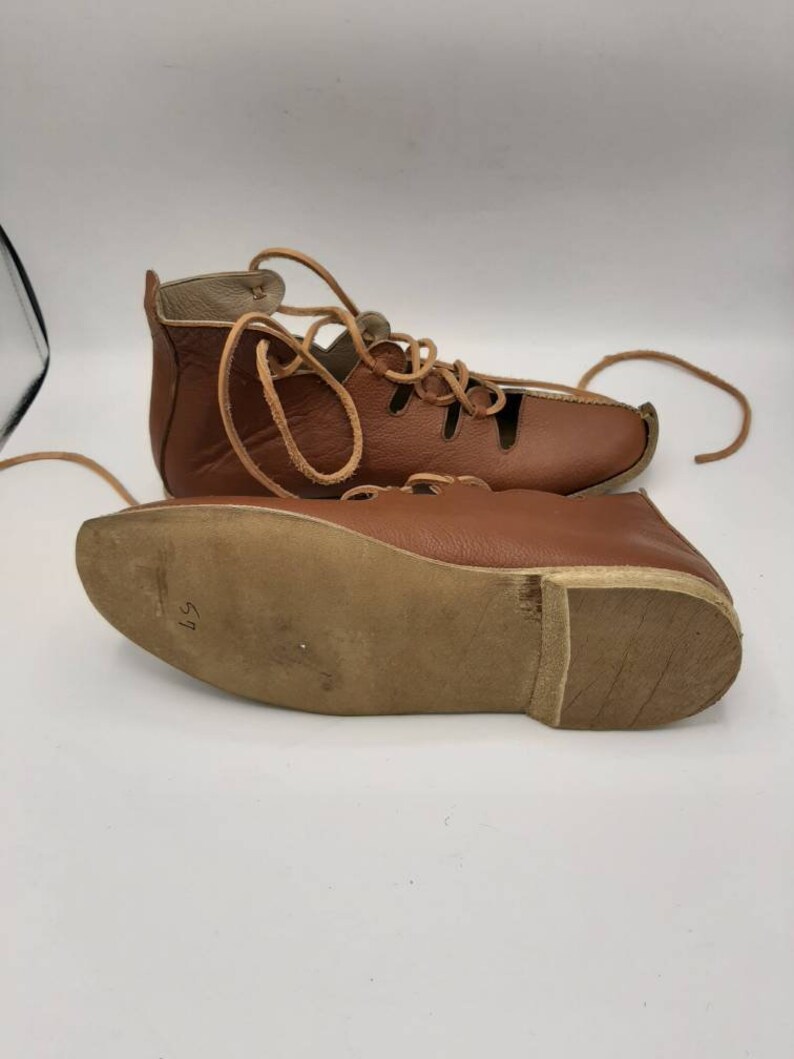 May include: Brown leather sandals with laces and cutouts. The sandals have a brown leather sole with the number 37 written on it.