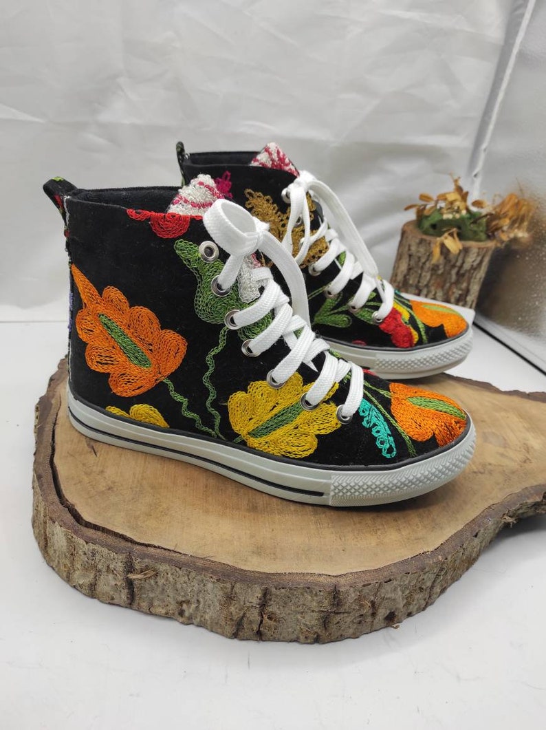 May include: Black high-top canvas shoes with colorful embroidered floral designs. The shoes have white laces and a white rubber sole.