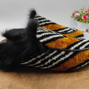 Puede incluir: Un par de zapatillas de estar por casa de rayas blancas y negras con una franja de terciopelo marr&oacute;n y ribete de piel negra.