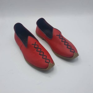 May include: A pair of red leather slip-on shoes with black stitching in a diamond pattern. The shoes have a pointed toe and a brown leather sole.