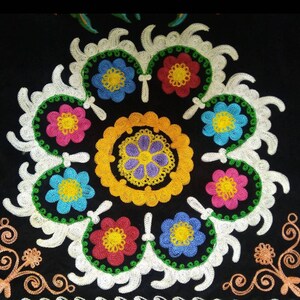 May include: A black fabric with colorful embroidered flowers in a circular pattern. The flowers are red, pink, yellow, blue, and green. The center of the circle has a yellow and purple embroidered design.
