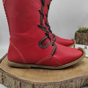 May include: Red leather boots with black laces and yellow stitching. The boots have a pointed toe and a flat sole.