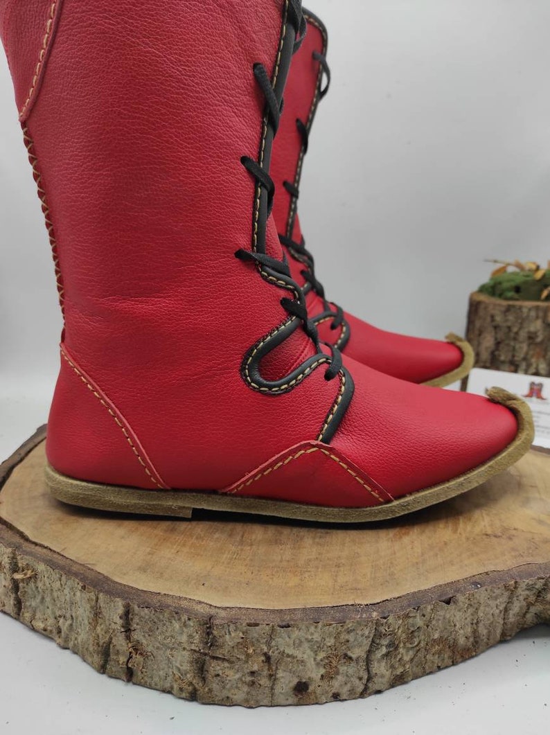 May include: Red leather boots with black laces and yellow stitching. The boots have a pointed toe and a flat sole.