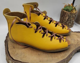 May include: A pair of yellow leather sandals with brown laces. The sandals have a cut-out design and are tied up the ankle.