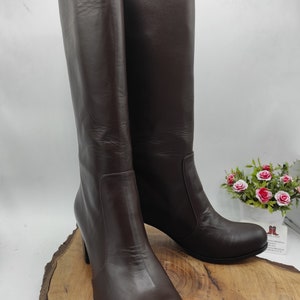 May include: A pair of brown leather knee-high boots with a low block heel. The boots have a platform toe and are made of smooth leather.