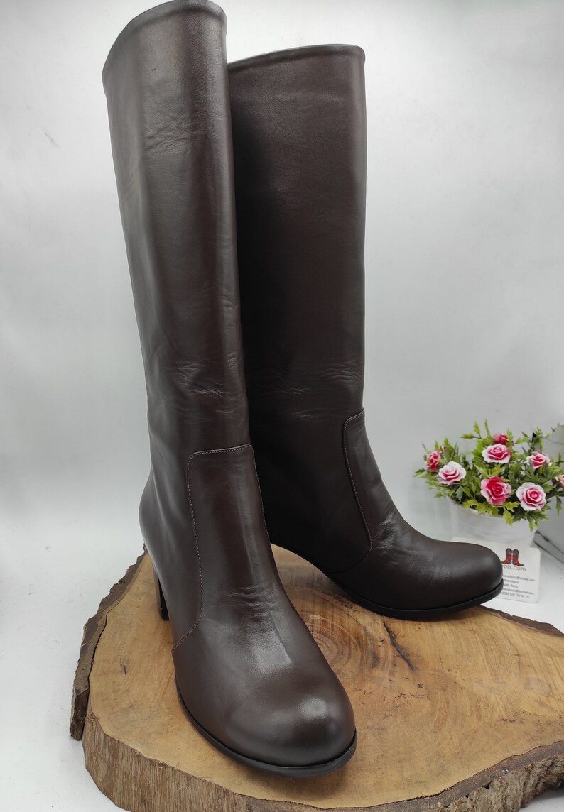 May include: A pair of brown leather knee-high boots with a low block heel. The boots have a platform toe and are made of smooth leather.