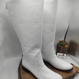 Puede incluir: Un par de botas blancas de cuero de ca&ntilde;a alta con punta puntiaguda y tac&oacute;n bajo de bloque. Las botas tienen una cremallera en el interior del tobillo.