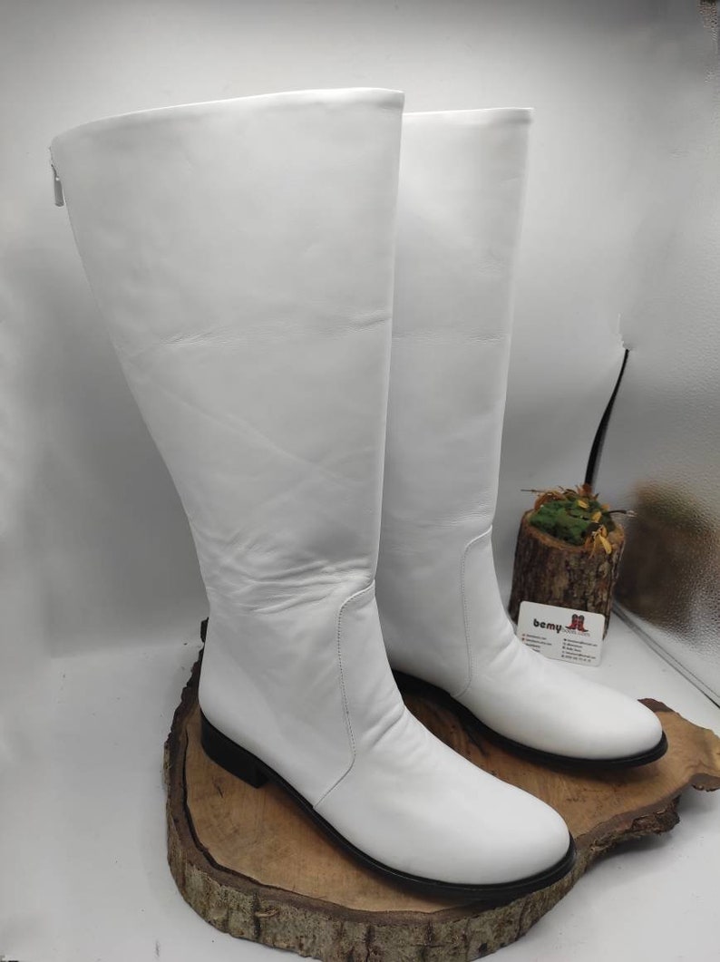 Puede incluir: Un par de botas blancas de cuero de ca&ntilde;a alta con punta puntiaguda y tac&oacute;n bajo de bloque. Las botas tienen una cremallera en el interior del tobillo.