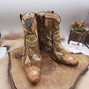 May include: A pair of brown suede ankle boots with floral embroidery. The boots have a pointed toe and a block heel.