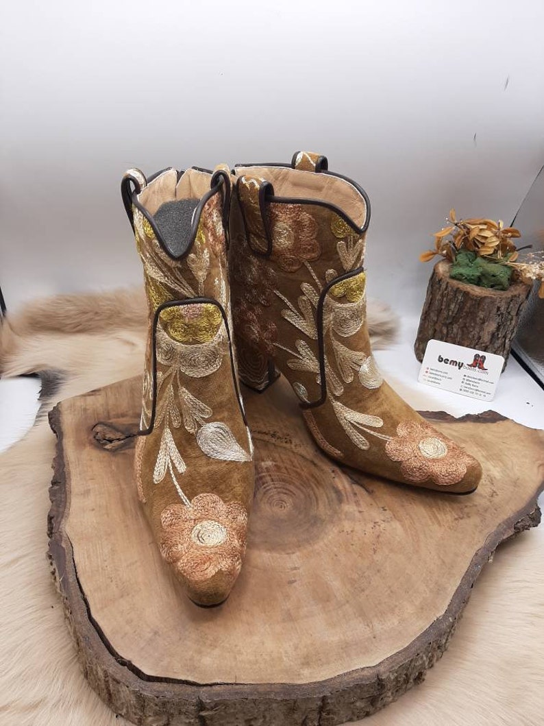 May include: A pair of brown suede ankle boots with floral embroidery. The boots have a pointed toe and a block heel.
