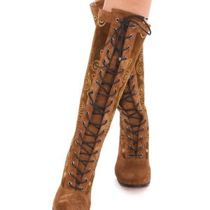 May include: Brown suede knee-high boots with gold embroidery and black laces.