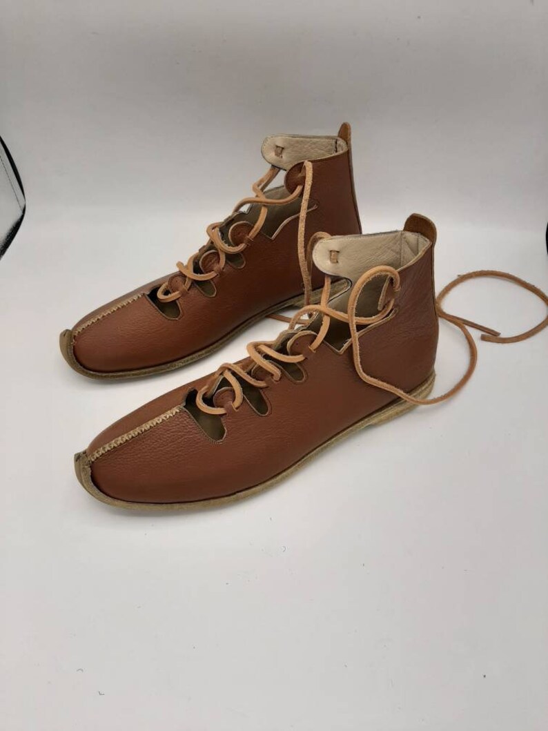 May include: Brown leather lace-up sandals with a cut-out design. The sandals have a flat sole and are tied at the ankle.