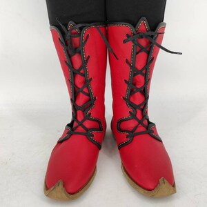 May include: Red leather boots with black laces and yellow stitching. The boots have a pointed toe and a brown sole.