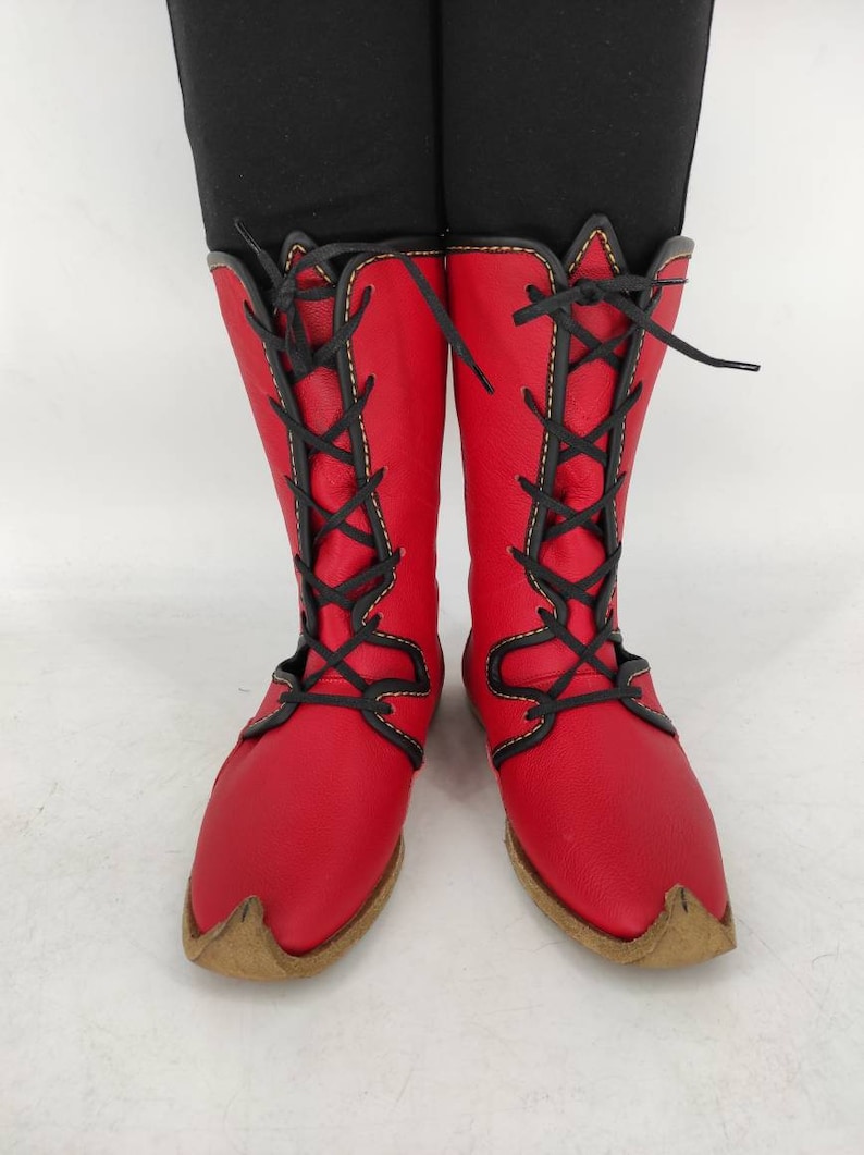 May include: Red leather boots with black laces and yellow stitching. The boots have a pointed toe and a brown sole.