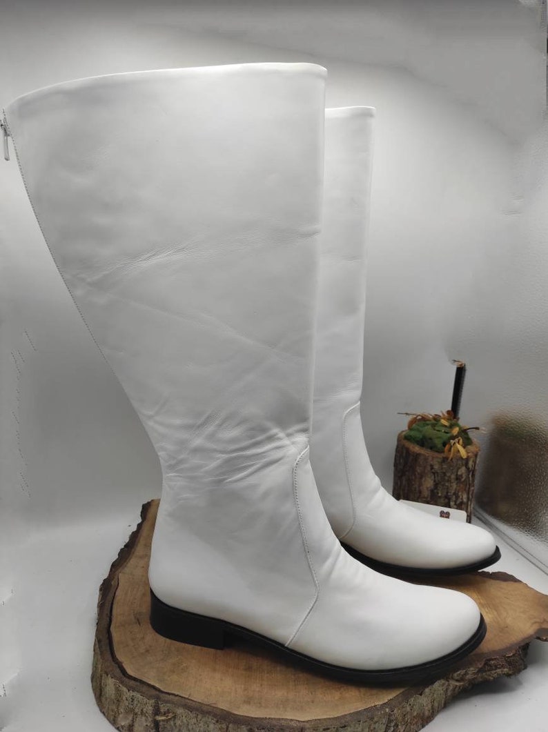 Puede incluir: Un par de botas blancas de cuero hasta la rodilla con tac&oacute;n bajo. Las botas tienen una cremallera en el interior de la pierna y una punta puntiaguda.