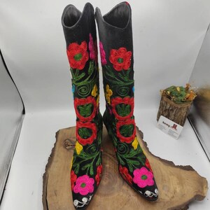 May include: A pair of black suede boots with colorful floral embroidery. The boots have a pointed toe and a low heel.