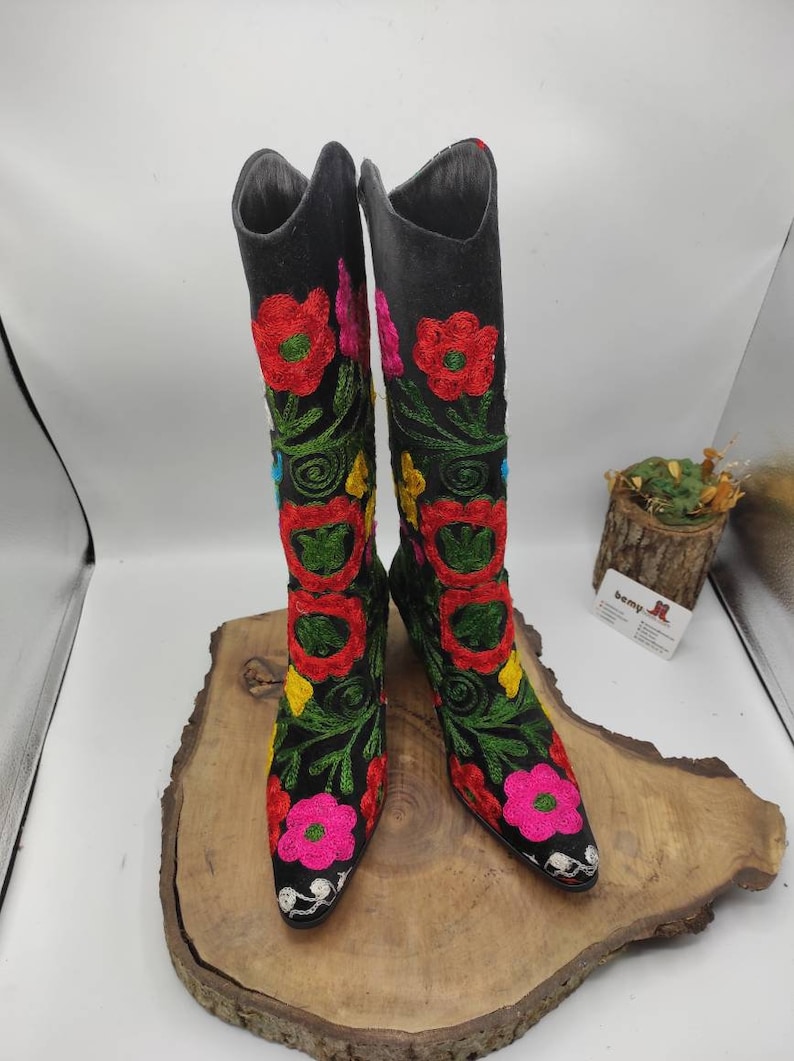 May include: A pair of black suede boots with colorful floral embroidery. The boots have a pointed toe and a low heel.