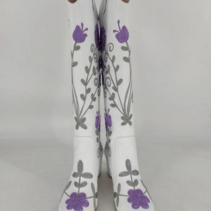 May include: White leather boots with a floral embroidery design. The flowers are purple and the stems are gray.