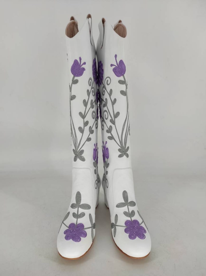 May include: White leather boots with a floral embroidery design. The flowers are purple and the stems are gray.
