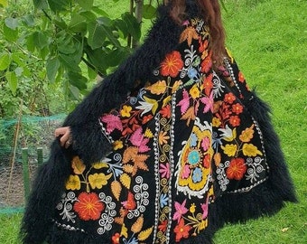 Op de afbeelding: Een zwart geborduurd jack met een pluche rand. De borduursels bevatten kleurrijke bloemenpatronen in tinten roze, geel, blauw en groen.