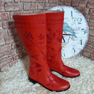 Puede incluir: Un par de botas rojas hasta la rodilla con intrincados bordados florales. Las botas presentan un acabado liso similar al cuero y una suela negra. El dise&ntilde;o incluye costuras detalladas y patrones decorativos, mostrando un estilo cl&aacute;sico. Altura: aprox. 40 cm.