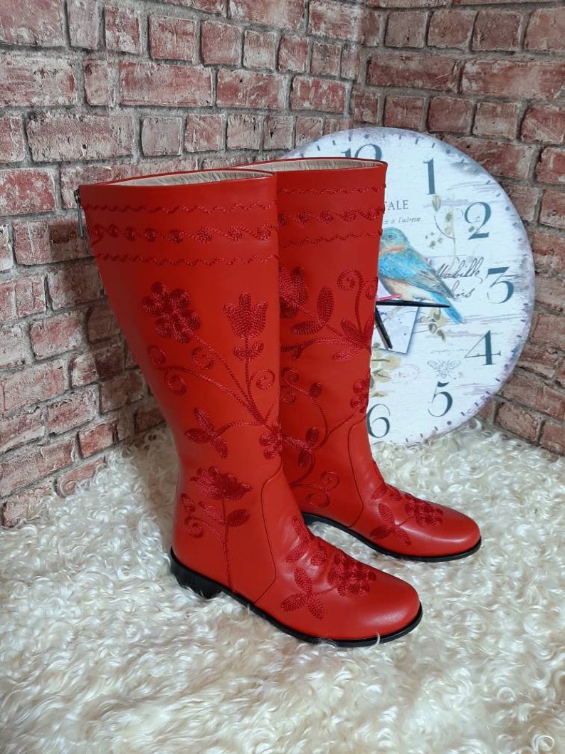 Puede incluir: Un par de botas rojas hasta la rodilla con intrincados bordados florales. Las botas presentan un acabado liso similar al cuero y una suela negra. El dise&ntilde;o incluye costuras detalladas y patrones decorativos, mostrando un estilo cl&aacute;sico. Altura: aprox. 40 cm.