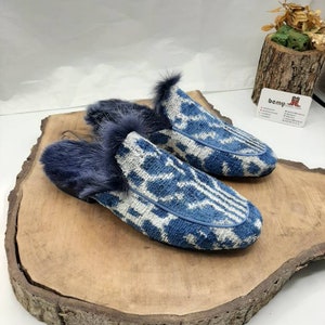 May include: A pair of blue and white patterned slippers with a fuzzy gray trim. The slippers are sitting on a wooden surface.
