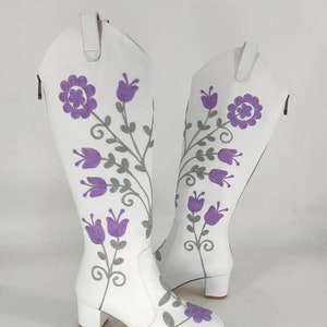 May include: White leather knee-high boots with a block heel and purple floral embroidery.