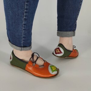 K&ouml;nnte beinhalten: Ein Paar orangefarbene und gr&uuml;ne Lederschuhe mit Stickereien. Die Schuhe haben eine Schn&uuml;rung vorne und eine spitze Zehenpartie.