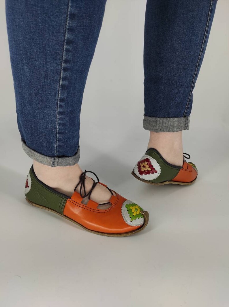 K&ouml;nnte beinhalten: Ein Paar orangefarbene und gr&uuml;ne Lederschuhe mit Stickereien. Die Schuhe haben eine Schn&uuml;rung vorne und eine spitze Zehenpartie.