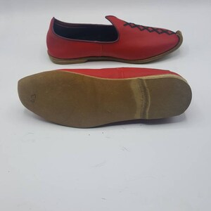 May include: Red leather slip-on shoes with black stitching and a brown leather sole. The sole is marked with the number "43".