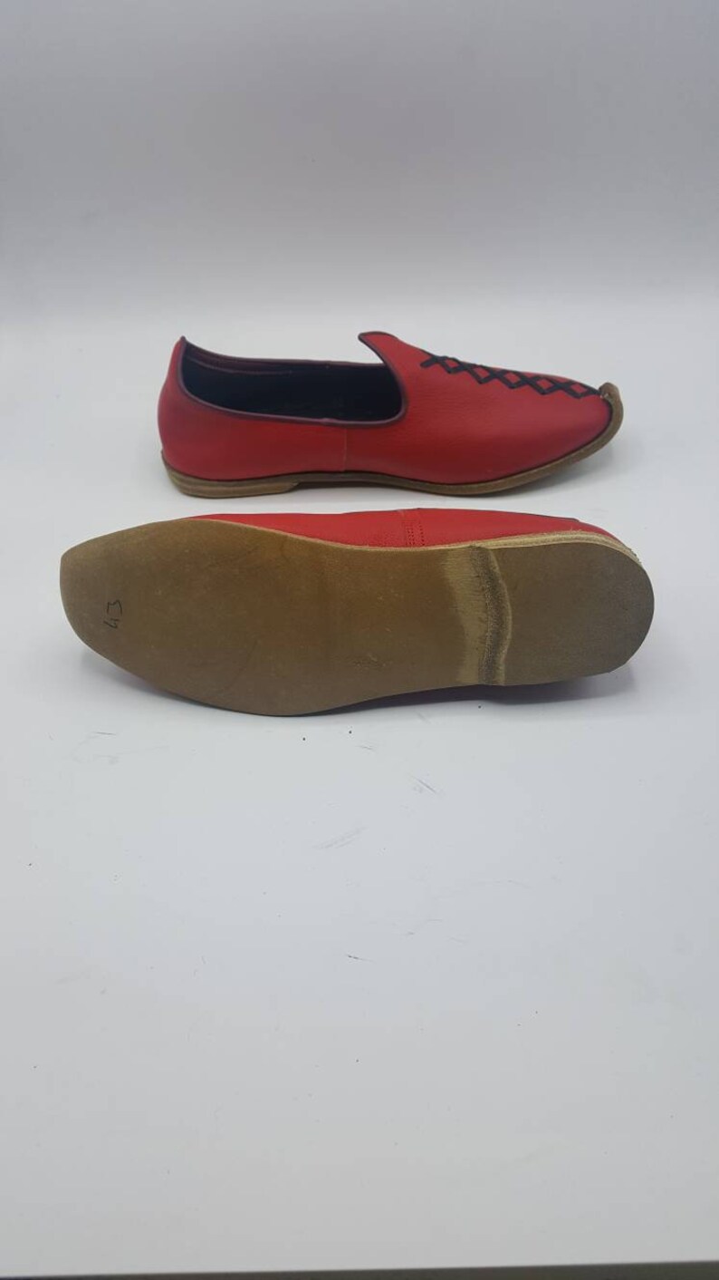 May include: Red leather slip-on shoes with black stitching and a brown leather sole. The sole is marked with the number "43".