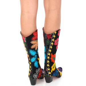 May include: A pair of black boots with colorful floral embroidery. The boots have a pointed toe and a block heel.