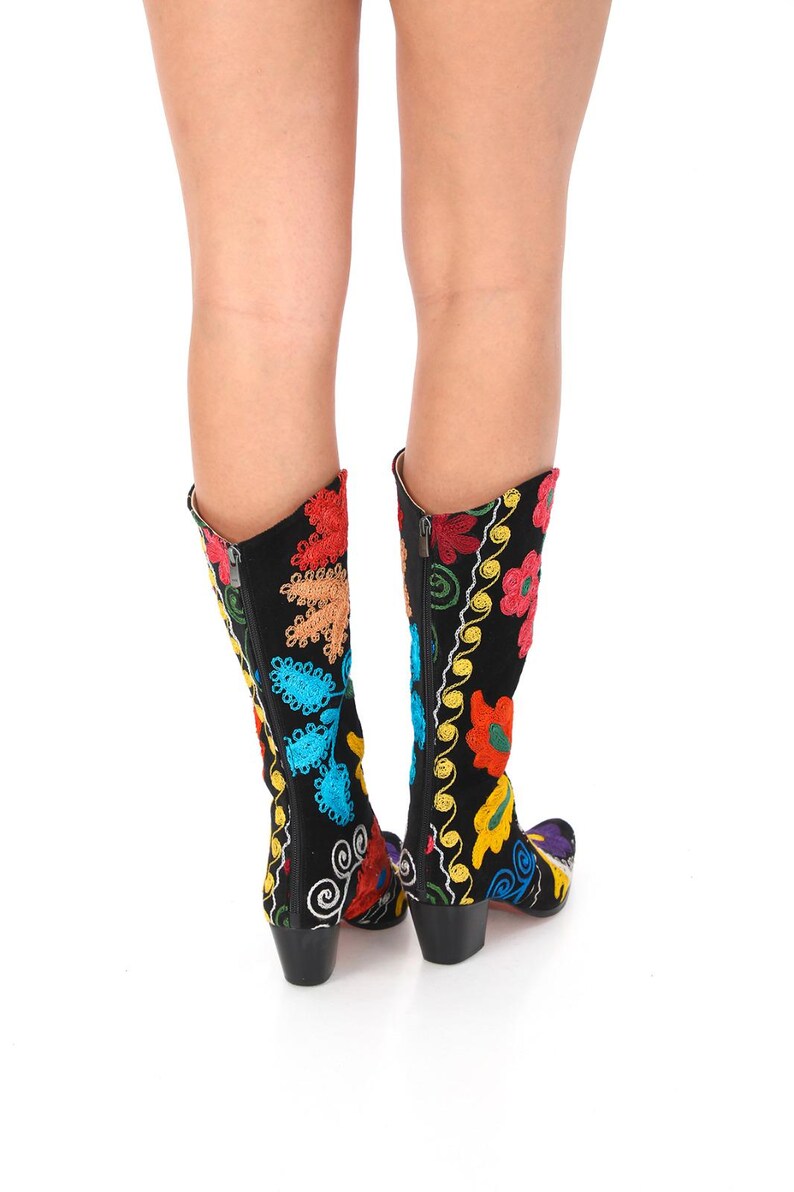 May include: A pair of black boots with colorful floral embroidery. The boots have a pointed toe and a block heel.