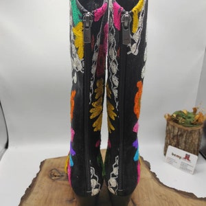May include: A pair of black suede boots with colorful embroidery. The boots have a zipper on the inside of each boot and a block heel.