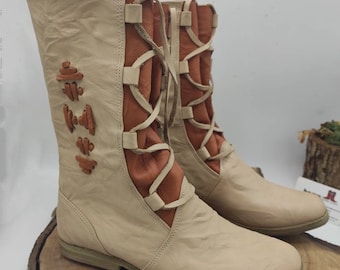 May include: A pair of beige leather boots with brown leather laces and decorative stitching. The boots have a rounded toe and a low heel.