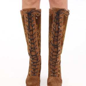 May include: Brown suede knee-high boots with gold embroidery and black laces.