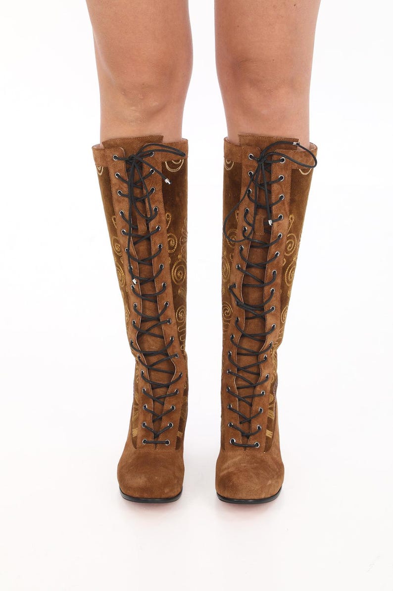 May include: Brown suede knee-high boots with gold embroidery and black laces.