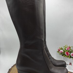 May include: A pair of brown leather knee-high boots with a block heel. The boots have a zipper on the inside of the ankle and a platform toe.