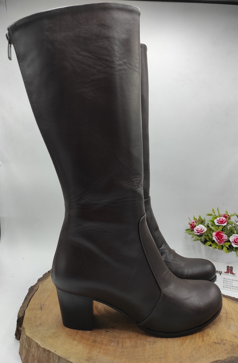 May include: A pair of brown leather knee-high boots with a block heel. The boots have a zipper on the inside of the ankle and a platform toe.