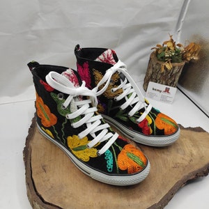 May include: A pair of black high-top canvas shoes with colorful embroidered flowers. The shoes have white laces and a white rubber sole.