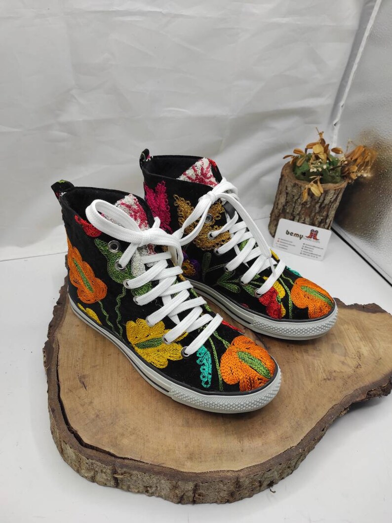May include: A pair of black high-top canvas shoes with colorful embroidered flowers. The shoes have white laces and a white rubber sole.