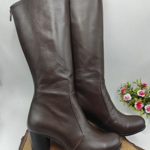 May include: A pair of brown leather knee-high boots with a block heel. The boots have a zipper on the back and a pointed toe.