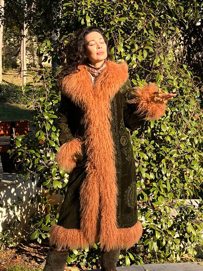 May include: A long, green velvet coat with a brown fur collar and cuffs. The coat has a paisley pattern and is lined with a brown fur.