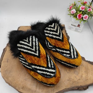 Puede incluir: Un par de zapatillas rayadas en blanco y negro con una parte superior de terciopelo marr&oacute;n y ribete de piel negra.
