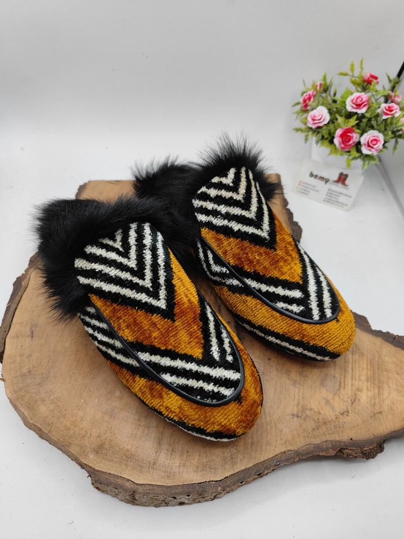 Puede incluir: Un par de zapatillas rayadas en blanco y negro con una parte superior de terciopelo marr&oacute;n y ribete de piel negra.